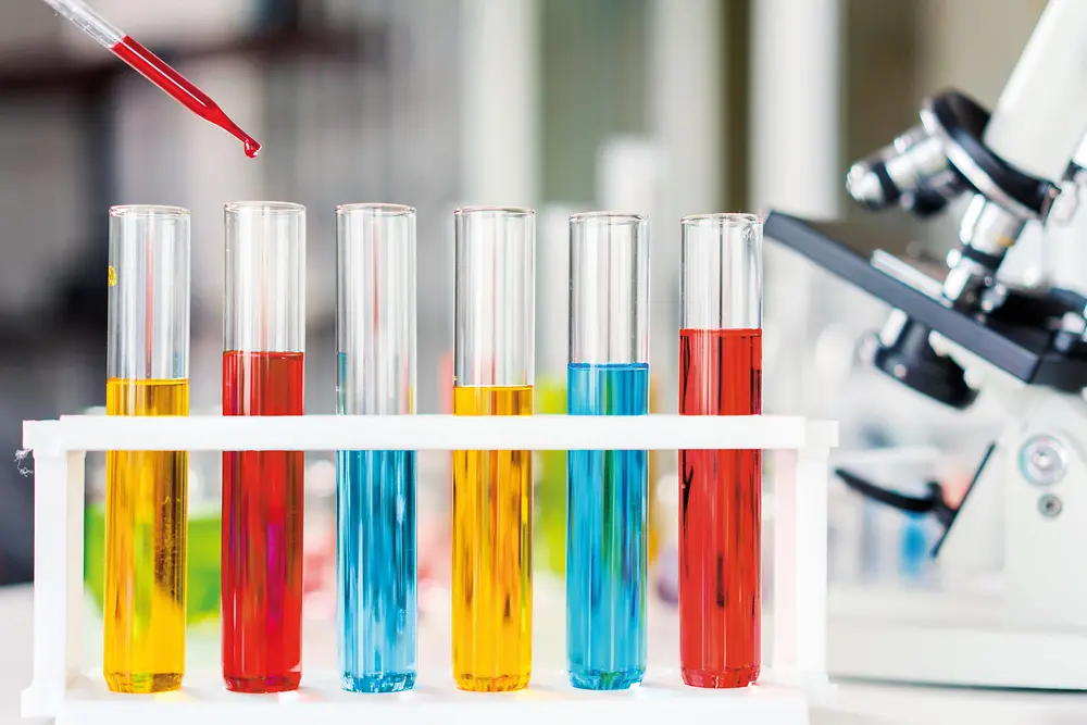 Test tubes are filled with red, yellow and blue liquids representing chemicals for evaluation and registration in the REACH context.